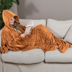 a woman is laying on a couch with a book in her hand and she is wearing an orange hooded blanket