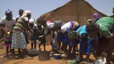 a group of people standing next to each other in front of a hut and buckets