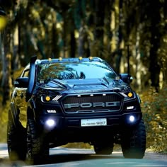 a black truck driving down a road next to trees