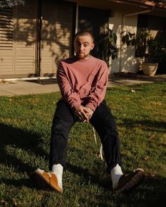 a man sitting on the grass in front of a house with his legs crossed and one foot up