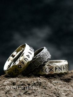 two wedding rings with roman writing on them sitting on top of a rock in front of a dark background