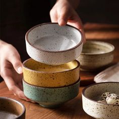 a stack of bowls sitting on top of a wooden table next to two hands reaching for one