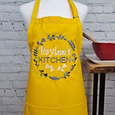 a yellow apron with baylee's kitchen on it next to a red bowl