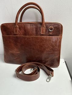 The 16 inch genuine leather laptop bag for men could have a stylish and sturdy design with durable stitching and quality metal accessories. It can have multiple compartments and pockets for organization, including a dedicated laptop compartment with a soft lining for protection. The straps could be adjustable for wearing comfort, and the genuine leather material would give it a refined look and durability. The design of the bag could be minimalist, with clean lines and subtle details, fitting an Leather Laptop Bag With Luggage Sleeve For Office, Office Leather Laptop Bag With Luggage Sleeve, Classic Leather Laptop Bag With Sleeve, Leather-backed Laptop Bag For Office, Rectangular Leather Laptop Bag For Office, Leather Laptop Bag With Sleeve In Satchel Shape, Brown Leather-backed Laptop Bag For Work, Leather Briefcase With Laptop Sleeve For Office, Leather-backed Rectangular Laptop Bag For Office