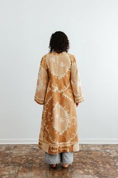 This semi-fitted duster was made from an antique hand-embroidered woven cotton Suzani, a textile traditionally used as wall hangings or in the yurts of nomadic people in Central Asia. An original aloka design, we prepared the vintage material with our signature multi-step shampoo and softening process. In our Athens, Georgia-based studio, our designers created this A-line semi fitted jacket with a plunging neckline and puffed bell sleeves. Served bound seams on the interior showcase the hand-stitching. Thick trim along the bottom of the jacket and sleeves give it a luxurious look and drape. Each textile bares memories and marks of the hand and past. Each piece is a one-of-a-kind garment. We carefully curate and prepare these beautifully preserved textiles and embrace imperfections, mending Beige Embroidered Bohemian Kurta, Bohemian Beige Embroidered Kurta, Traditional Brown Cotton Kaftan, Bohemian Kurta With Woven Motifs, Bohemian Brown Cotton Kurta, Traditional Long Brown Kurta, Traditional Cotton Ikat Print Kimono, Traditional Cotton Kimono With Ikat Print, Bohemian Long Kurta With Intricate Embroidery