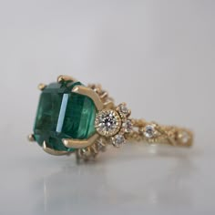 an emerald and diamond ring on a white surface