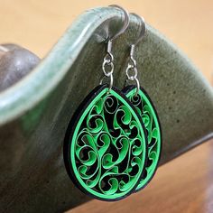 a pair of green and black earrings sitting on top of a wooden table next to a vase