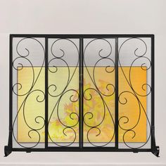 a black iron gate with yellow and orange painting behind it on a white wall in front of a window