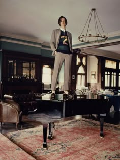 a man standing on top of a piano in a living room next to a chandelier