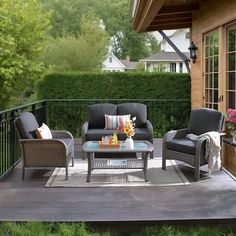 an outdoor living area with furniture and flowers on the table, in front of a wooden deck