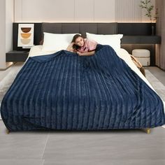 a woman laying on top of a bed covered in a blue bedspread and blanket