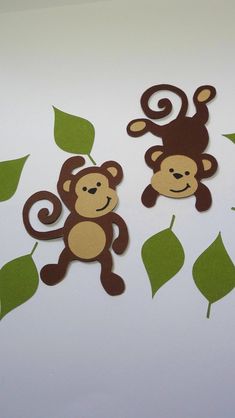 two monkey cutouts sitting next to each other on top of a white table with green leaves