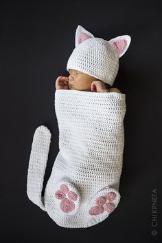 a baby sleeping in a white crochet cat blanket with pink paws on it