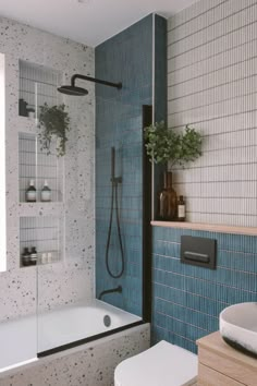 a bathroom with blue tiles and a white toilet next to a bathtub in the corner