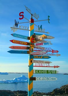 a pole with many different signs on it by the water and icebergs in the background