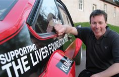 a man sitting on the side of a red car with his hand out and smiling