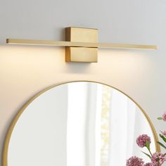 a round mirror sitting on top of a wall next to a vase with flowers