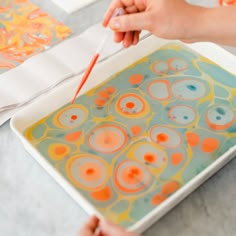 someone is painting on a tray with orange and blue circles