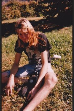 a man sitting in the grass with his legs crossed and one hand on his knees