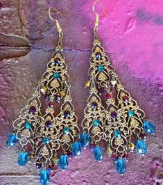 "These Antique Brass Filigree Moroccan Boho Chandelier Earrings are made with brass filigrees tiered to form a beautiful classic chandelier shape. Colorful crystal beads hang on each tier. Swarovski rhinestones add a touch of sparkle! Available with Posts, Clip-Ons, Leverbacks or French Wires. -4 1/2\" Long x 1 3/4\" Wide -0.4 oz. ea. Metal Finishes Available: -Antiqued Brass (as pictured) -Aged Bronze -Silver *As seen in the video Images show the 'Peacock Teal and Garnet', 'Ruby Red' & 'Bla Festive Bohemian Jeweled Earrings, Bohemian Jeweled Beaded Drop Earrings, Jeweled Drop Chandelier Earrings For Festivals, Bollywood Style Dangle Chandelier Earrings With Intricate Design, Handmade Ornate Chandelier Earrings For Festive Occasions, Bohemian Chandelier Earrings For Weddings And Festivals, Festive Bohemian Dangle Chandelier Earrings, Festive Bohemian Chandelier Earrings With Dangling Beads, Gold Bohemian Crystal Earrings For Wedding