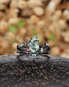 a ring with green and white stones sitting on top of a black piece of metal