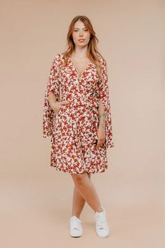 a woman in a red and white floral print dress standing with her hands on her hips