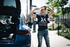 a woman standing next to a blue car with her hands on her head and looking at the ground