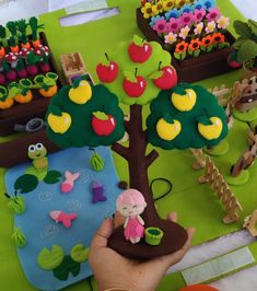 a hand is holding an apple tree in front of some fake trees and other decorations