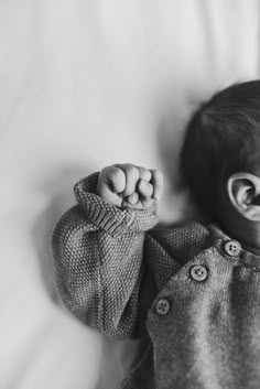 a black and white photo of a baby holding his hands up in the air while laying on a bed