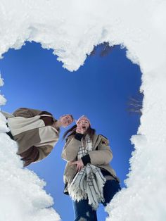 two people are standing in the snow making a heart shape