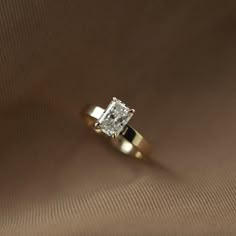 an engagement ring with a princess cut diamond in the center on a brown background,