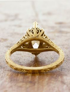 an antique style diamond ring with filigrees on the sides, sitting on a wooden surface