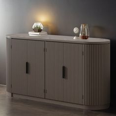 a sideboard with three doors and two vases on the top, against a gray wall