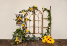 yellow flowers and greenery are arranged in front of an old window on a wooden floor