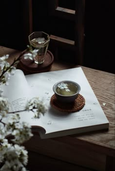 an open book on a table with a bowl of soup in front of it and flowers