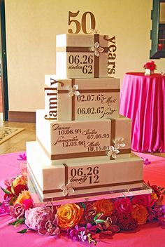 a wedding cake sitting on top of a table covered in pink and orange flowers next to a red table cloth