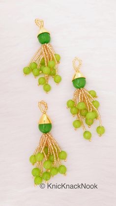 two green and gold earrings with beads on them, one is dangling from the side