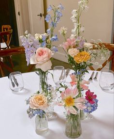 three vases filled with flowers sitting on top of a white tablecloth covered table