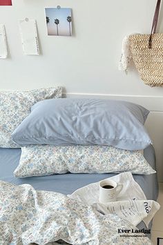 an unmade bed with blue sheets, pillows and a basket hanging on the wall