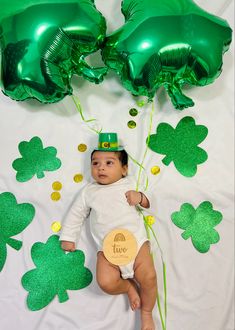 a baby in a st patrick's day outfit laying on the ground with green balloons