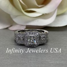 a white rose sitting next to a diamond ring on top of a table with the words infinitity jewelers usa