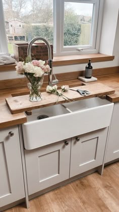 a kitchen with white cabinets and wooden counter tops, flowers in a vase on the window sill