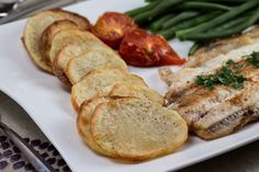 a white plate topped with fish and potatoes next to green beans, tomatoes and cherry tomatoes