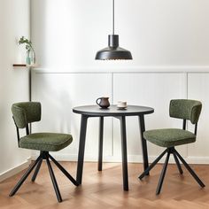 two green chairs sitting at a small round table with a black lamp hanging over it