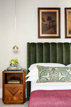 a bed with green velvet headboard and two pictures on the wall next to it