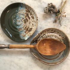 two bowls with wooden spoons sitting on top of a marble counter next to dried flowers