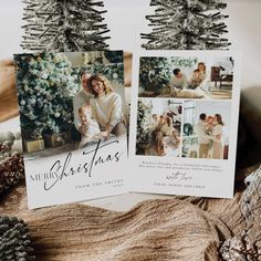 two christmas cards sitting on top of a wooden table next to pine cones and fir trees