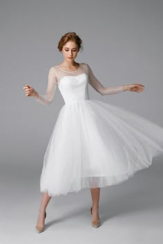 a woman wearing a white dress with sheer sleeves and tulle on the skirt is posing in