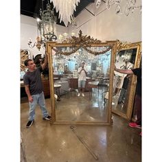 a man standing in front of a large mirror next to a chandelier hanging from the ceiling