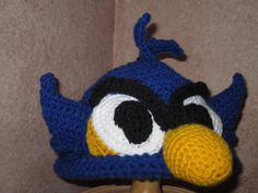 a crocheted blue bird hat on top of a wooden stand in front of a wall